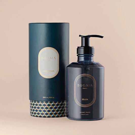 Elegantiškas ZELDA prabangus rankų muilas 250 ml talpos buteliuke su dozatoriumi. Stilingas dizainas su subtiliomis gėlių ir medienos natomis, puikiai tinkantis vonios ar virtuvės interjerui. Fone – švarus, modernus paviršius.